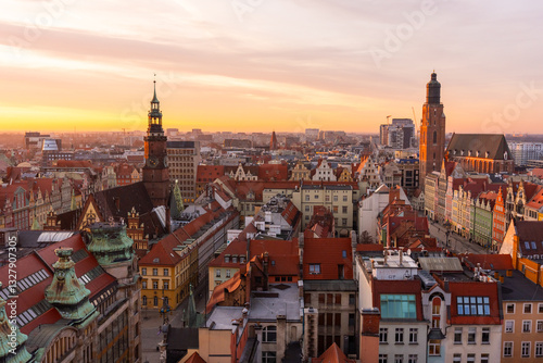 Scenic aerial view of historic European city at sunset with colorful rooftops, old town architecture, and church towers. Warm golden light enhances the charm of the picturesque urban landscape.