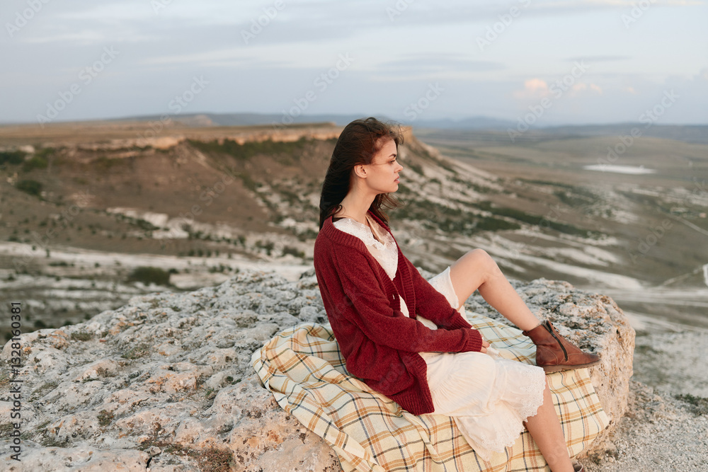 Woman sitting on a blanket enjoying scenic valley view from mountain top on a travel adventure Woman sitting on a blanket enjoying scenic valley view from mountain top on a travel adventure