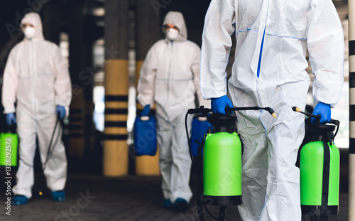 Warning, coronavirus disinfection. Men in virus protective suits carrying spray bottles with chemicals, blurred background