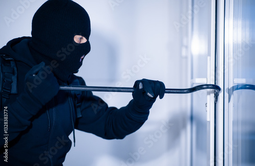 Intrusion Concept. Side view portrait of disguised prowler breaking house or office door with crowbar