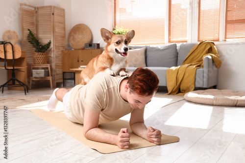 Sporty young redhead man with cute Corgi dog training on yoga mat at home