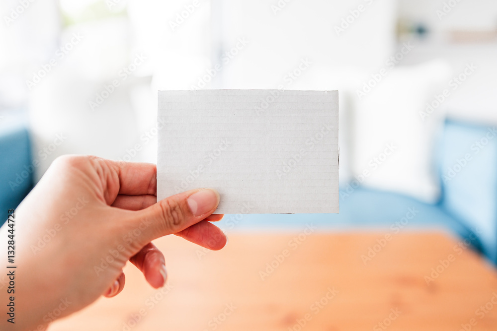 hand holding small cardboard label with blank copy space in front of stylish sofa and coffee table hand holding small cardboard label with blank copy space in front of stylish sofa and coffee table
