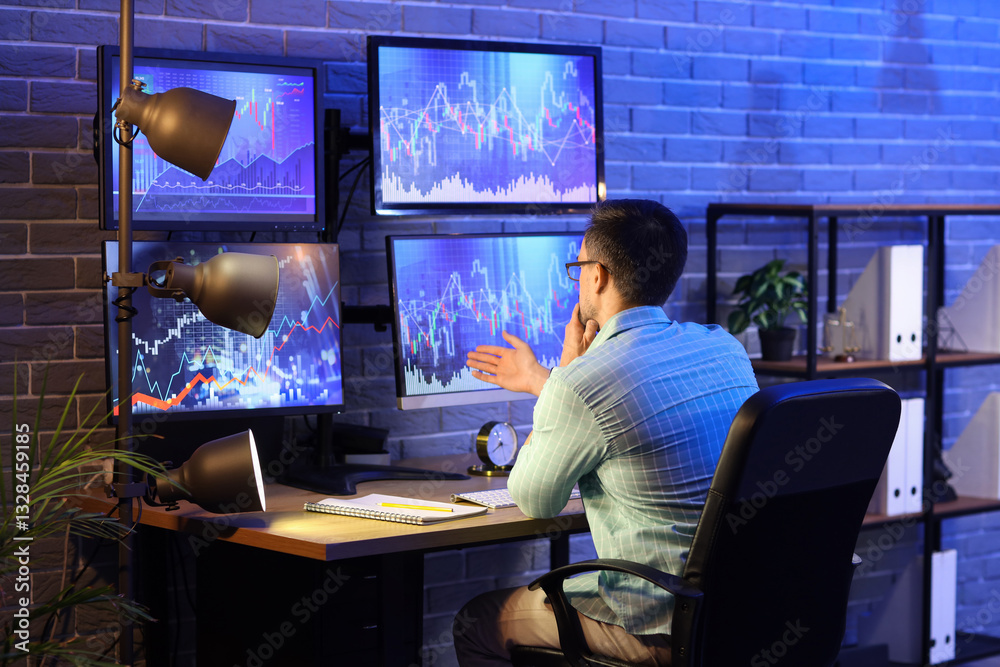Male trader working in office at night, back view Male trader working in office at night, back view