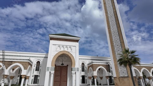 Wide angle view of the Masjid Lalla Abosh mosque in Tangier, Morocco, featuring its white facade, arches and minaret under a cloudy blue sky