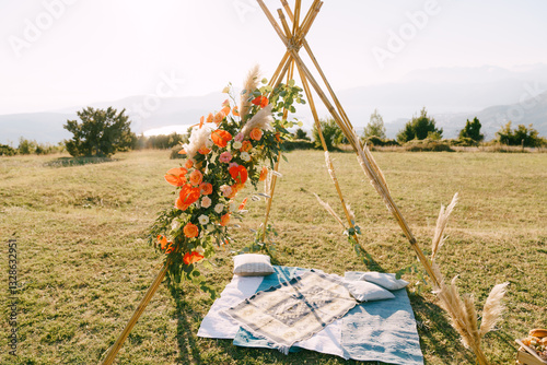 Wedding arch-wigwam stands over homespun bedspreads and pillows on a green meadow in the mountains