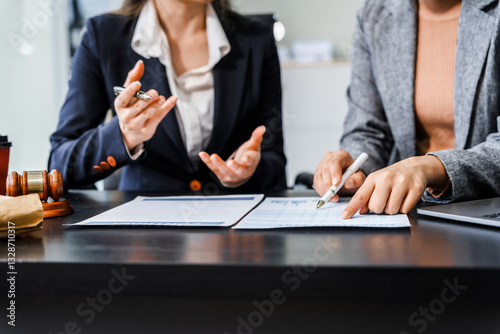 Two female lawyers in business suits meet at wooden desk, shaking hands over contract paper. wooden gavel and scales justice as discuss legal compliance, corporate law, dispute resolution.
