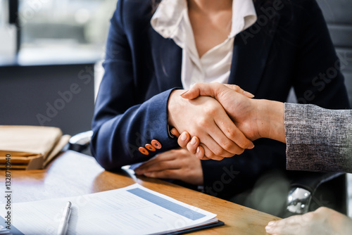 Two female lawyers in business suits shake hands at wooden desk, finalizing legal agreement. wooden gavel and scales represent justice as they discuss corporate law, compliance, dispute resolution.