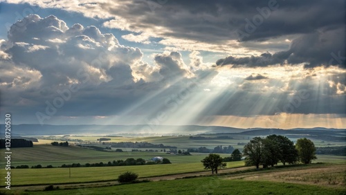 Sunbeams piercing through clouds over a tranquil rural landscape.