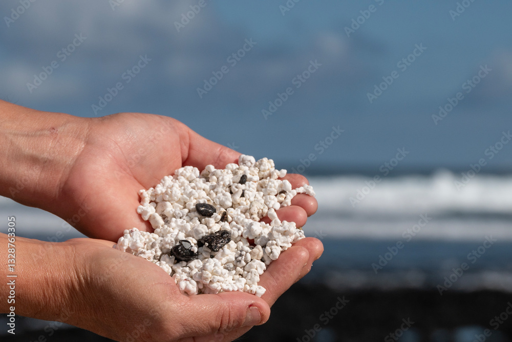 Manos de chica sosteniendo piedritas blancas con forma de popcorn mezcladas con piedras negras volcánica. Fuerteventura.