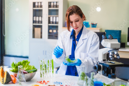 Middle-aged female laboratory worker wearing blue gloves conducts lab test on food ingredients lettuce, cucumber, pork. Using microscope, she analyzes nutrients, preservatives, food safety records.