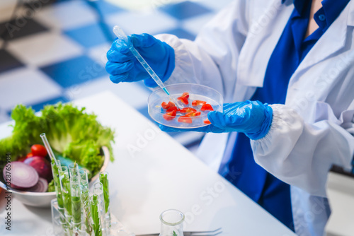 Middle-aged female laboratory worker wearing blue gloves conducts lab test on food ingredients lettuce, cucumber, pork. Using microscope, she analyzes nutrients, preservatives, food safety records.