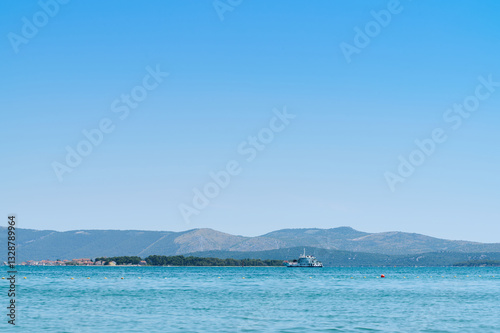 Bright blue sky above serene waters with small boat near an island on a sunny day, showcasing coastal beauty.