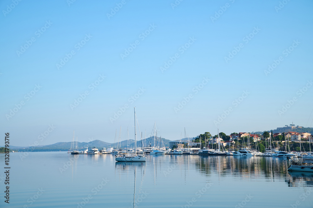 Sailboats are anchored peacefully in a serene harbor against a backdrop of distant hills and clear blue sky. Sailboats are anchored peacefully in a serene harbor against a backdrop of distant hills and clear blue sky.
