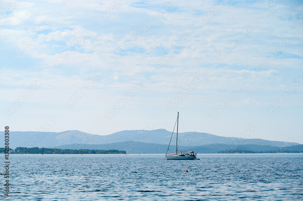 Naklejka premium A sailboat moves gracefully on calm waters surrounded by elegant mountains and a bright sky.