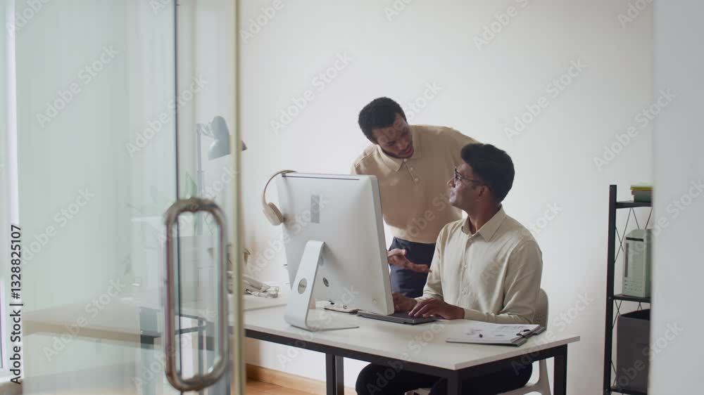 Medium long shot of two diverse male coworkers developing business plan on computer at desk in modern office Medium long shot of two diverse male coworkers developing business plan on computer at desk in modern office