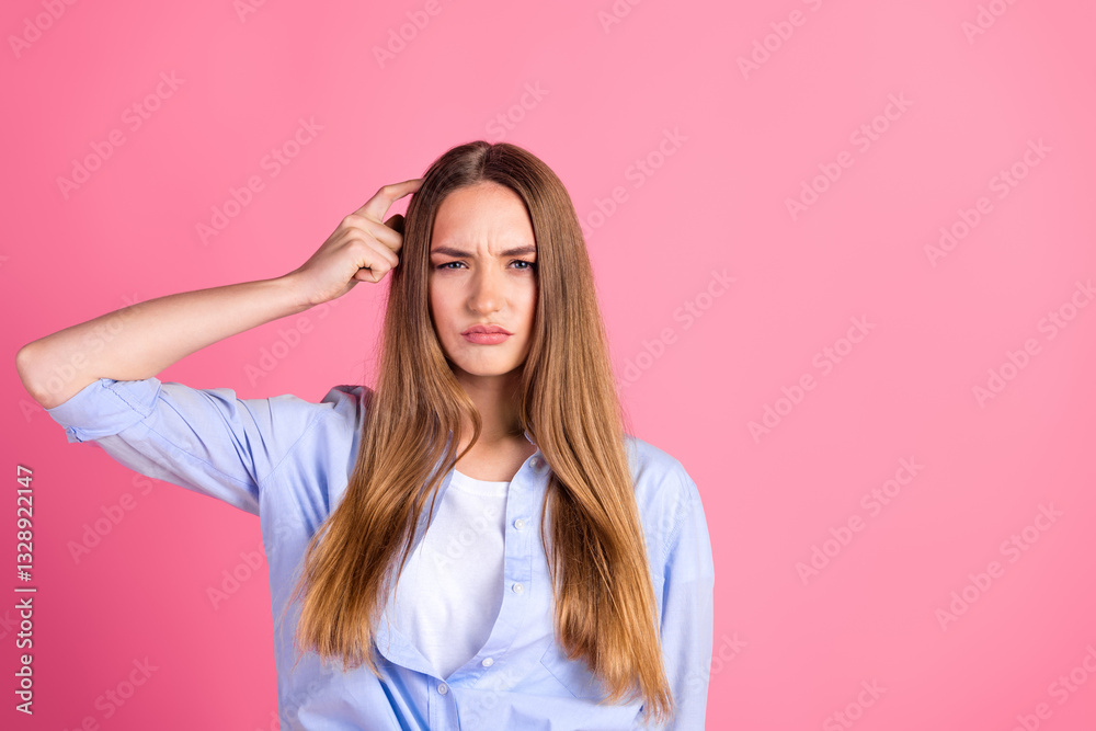 Young woman with thoughtful expression, touching her head, standing against pink background wearing a casual blue shirt Young woman with thoughtful expression, touching her head, standing against pink background wearing a casual blue shirt