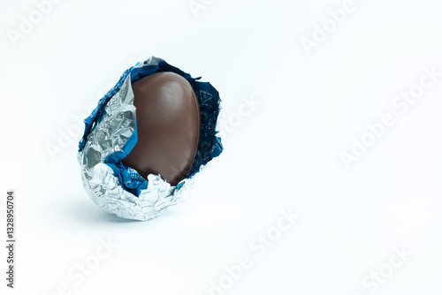 Φωτογραφία A partially unwrapped chocolate Easter egg with silver and blue foil on a white background