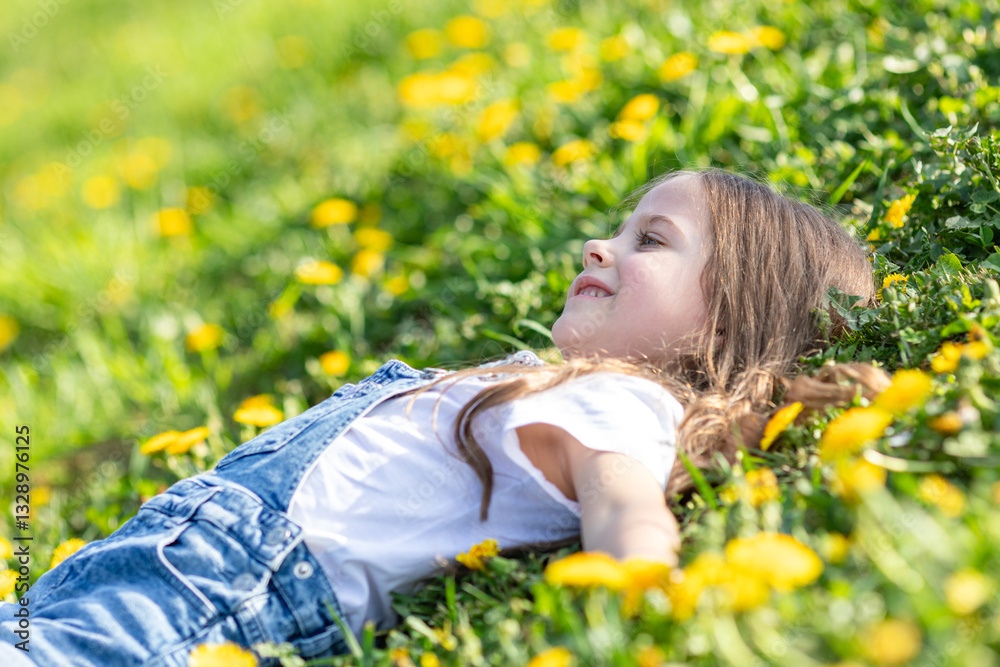 Portrait of little cute girl lying with dandelions on the grass. Happy smiling girl lies on the grass among yellow flowering dandelions in the park. Spring concept. Happy life without allergy. Freedom Portrait of little cute girl lying with dandelions on the grass. Happy smiling girl lies on the grass among yellow flowering dandelions in the park. Spring concept. Happy life without allergy. Freedom