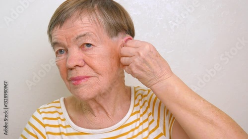 An elderly woman puts a hearing aid on her ear. Problems of aging and deafness. The use of medical technologies to support the hearing of elderly people with disabilities