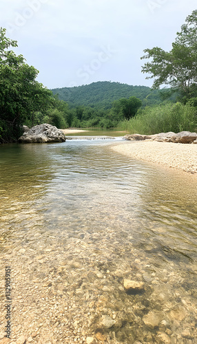 Serene shallow river flowing through a rocky, sandy bed, leading to lush green hills under a cloudy sky