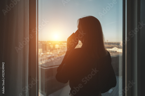 Silhouette of a woman talking on the phone by the office window.