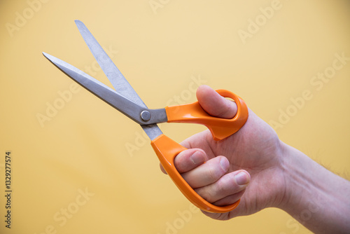 hand holding pair of scissors on yellow background