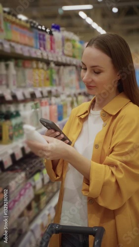Wallpaper Mural A shopper scans a bottle of liquid soap using her smartphone while browsing in a store aisle. She examines products on the shelves around her for information and pricing. Torontodigital.ca