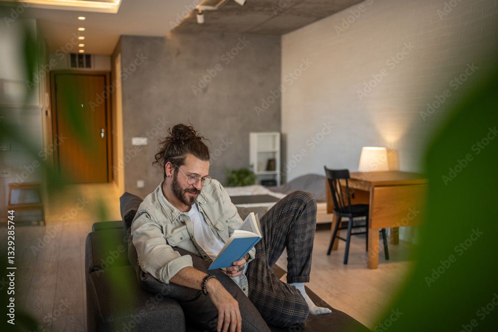 Young man reading a book on sofa in modern apartment Young man reading a book on sofa in modern apartment