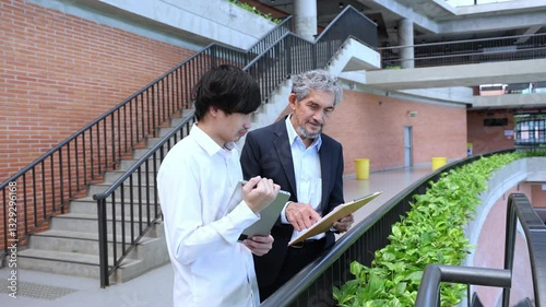 Asian senior professor is giving advice  to the college student on the research thesis while walking in the university faculty campus for education, academic and business concept