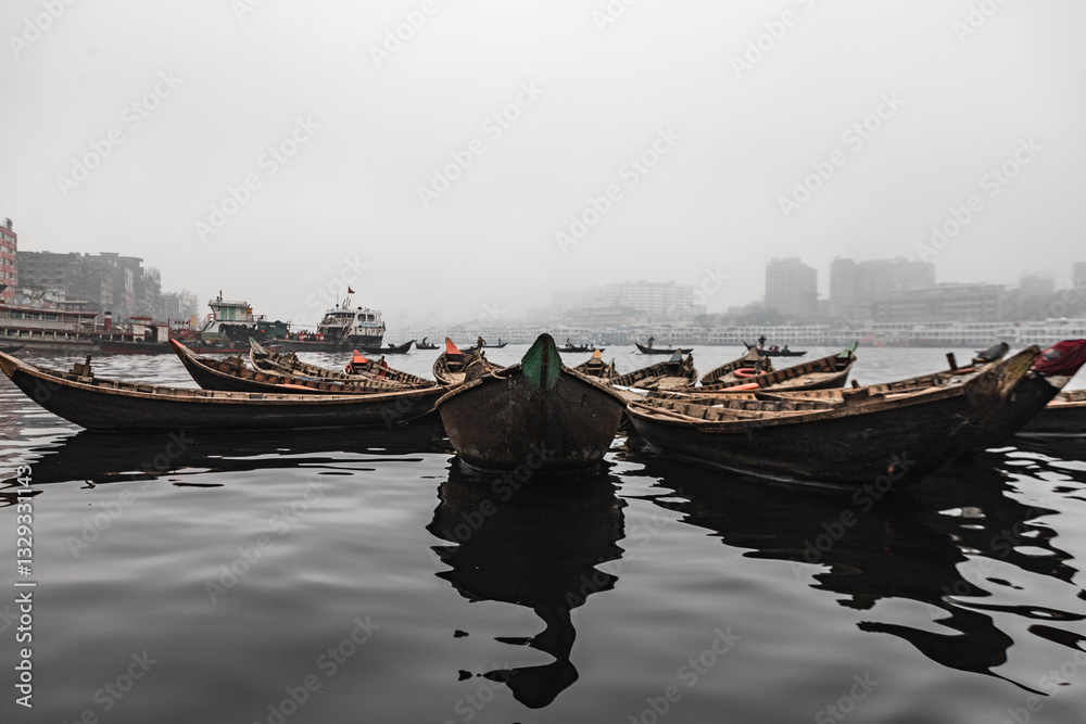 View of traditional wooden boats docked at the Buriganga river shipyard with a calm and overcast sky, Dhaka, Dhaka Province, Bangladesh. View of traditional wooden boats docked at the Buriganga river shipyard with a calm and overcast sky, Dhaka, Dhaka Province, Bangladesh.