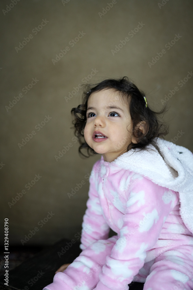 Close-up portrait of a little toddler girl with brown curly hairs and fluffy jumpsuit Close-up portrait of a little toddler girl with brown curly hairs and fluffy jumpsuit