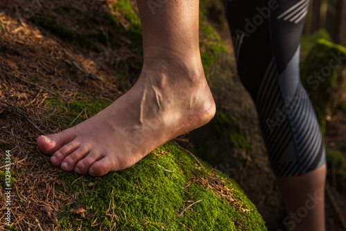 Young womans barefoot feet walking on moss and stone on forest, side view. Mental, healthy lifestyle background, go barefoot day