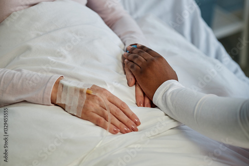 Hands of a patient with an IV drip being held by another person, conveying support and solidarity in a hospital setting