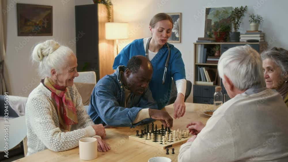 Elderly friends playing chess at wooden table while female caregiver in blue uniform assisting them during game in warmly lit living room of nursing home