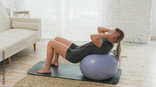 Young caucasian woman doing abdominal exercises while lying on her back on a gym ball in a bright room. The concept of a healthy lifestyle. Sports.