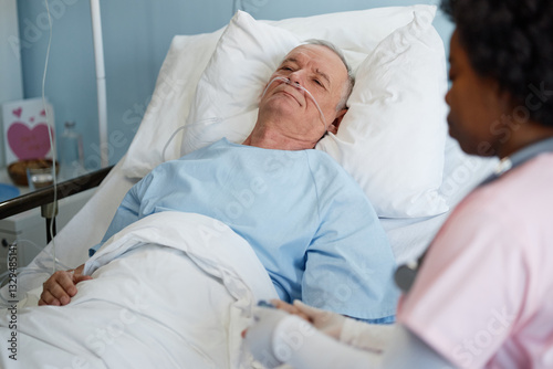 Elderly man lying in hospital bed with attendant nearby discussing medical details, sharing empathy and care for patients well-being, and critical health recovery photo