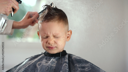 Young boy grimacing while a barber trims his hair. The child squints his eyes tightly in displeasure. Time for a Haircut
