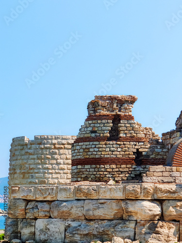 Part of dilapidated fortress stone wall of ancient fortress against background of blue clear sky. Weathered limestone. Copy space for text.