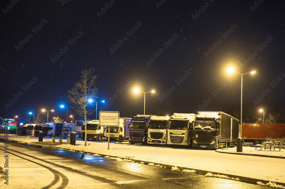 Lkw`s im Winter bei Schneefall auf einem Parkplatz bei Nacht