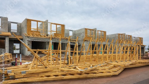Prefabricated wooden roof trusses stacked in front of a row of townhouses under construction in a suburban residential development on a cloudy afternoon in southwest Florida