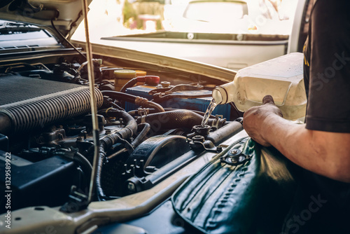 Male professional mechanic pouring antifreeze coolant liquid into car engine radiator in service center, car repair shop. Concept of car radiator coolant maintenance