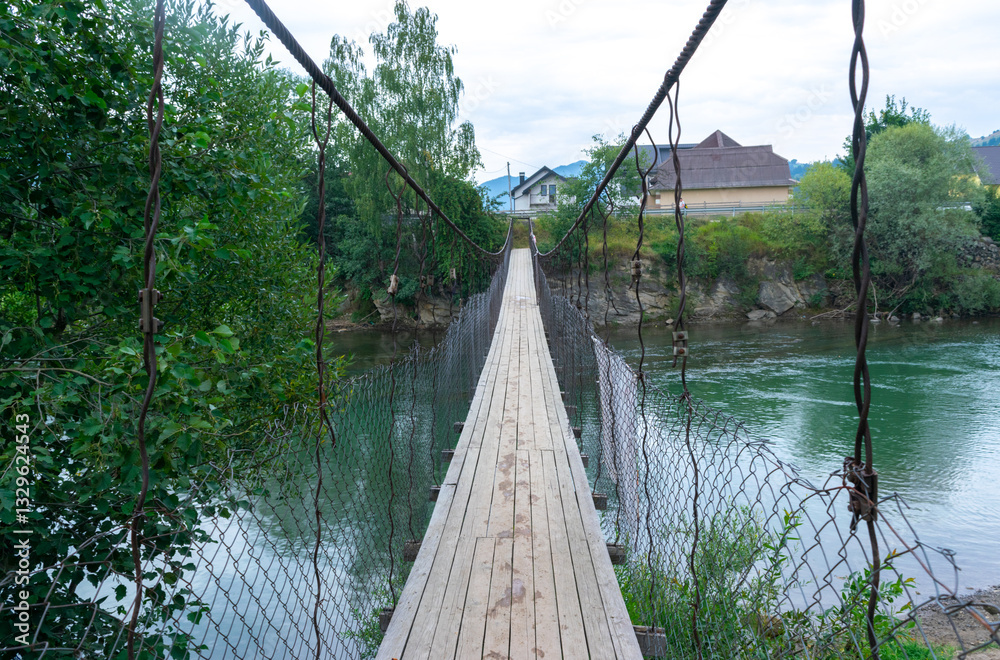 Fototapeta premium Narrow suspension wooden bridge across the Black Cheremosh River in the village of Verkhovyna. Ukraine.