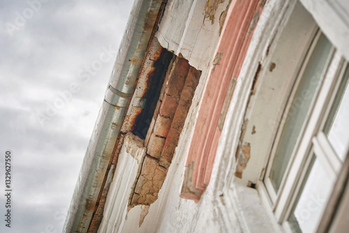 Obraz na płótnie Neglected historic building with crumbling cornice, missing plaster, and exposed bricks, architectural decay. Damaged building exterior with worn plaster and visible hole in the roof cornice w salonie