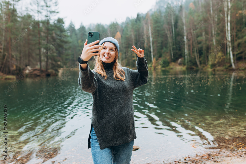Happy blonde Woman makes selfie mobile photo enjoying mountain lake landscape. Nature freedom adventure, vacation video call, girl tourist outdoors. Concept of an active lifestyle