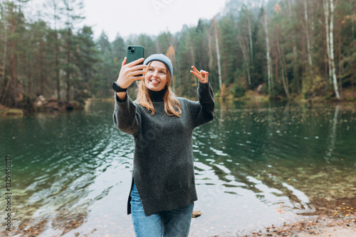 Obraz na płótnie Happy blonde Woman makes selfie mobile photo enjoying mountain lake landscape. Nature freedom adventure, vacation video call, girl tourist outdoors. Concept of an active lifestyle w salonie