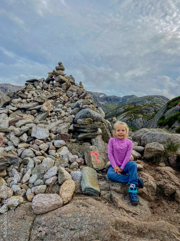 Naklejka premium Girl sitting by stone cairns on the Kjerag trail in Norway, hiking scene 