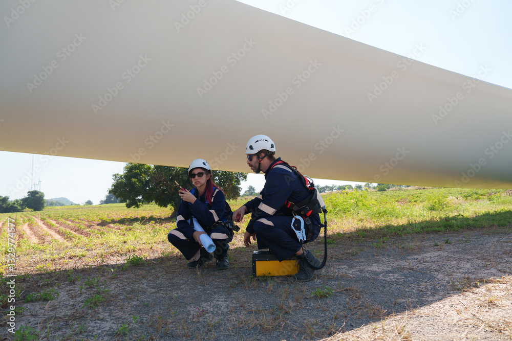 An engineer carefully examines a wind turbine blade at a construction site, placing a large blade on the ground to highlight the renewable energy technology. An engineer carefully examines a wind turbine blade at a construction site, placing a large blade on the ground to highlight the renewable energy technology.