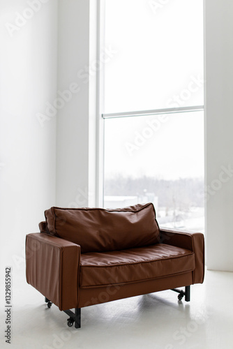 A brown leather faux-leather loveseat is positioned in a bright, white room.