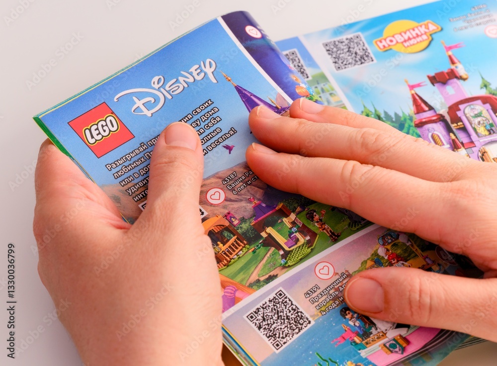 Obraz premium Tambov, Russian Federation - December 21, 2021 Woman browsing a Lego catalog on the page with Lego Disney sets.