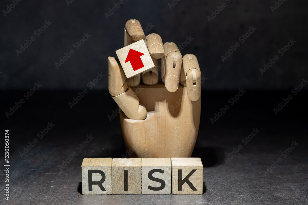 sztuczna ręka trzymająca kostkę z czerwoną strzałką w górę nad napisem na kostkach: RISK. Koncepcja zarządzania ryzykiem.